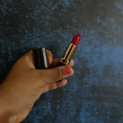 Holding up my handmade lipstick in a classic red shade. The gold and black packaging feels luxurious, but the formula inside is all-natural.