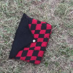 A top-down view of the checkered book sleeve on the grass. It's made from soft yarn to cushion your book.