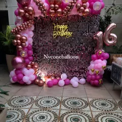 A glamorous 16th birthday celebration featuring a sparkling pink sequin wall. The setup is completed with a pink and rose gold balloon frame, a 'Happy Birthday' neon sign, and a large marquee number '16'.