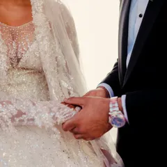 A close-up of the moment their hands meet. The bride's intricately beaded gown and the groom's classic tuxedo watch are details that tell the story of their personal style on their wedding day.