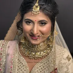 A stunning portrait of a Gujarati bride. The makeup features soft, shimmering eyeshadow and a warm lip color that beautifully complements her intricate gold jewellery and white lehenga.
