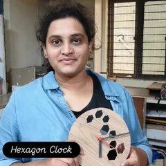 A student proudly holds the hexagon clock she designed and built. The clock face features cut-out geometric shapes for a modern, minimalist aesthetic.