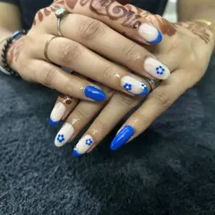 Adding a pop of color to a French manicure. This design features a vibrant blue French tip on an almond-shaped extension, with tiny, hand-painted white flowers for a cute, summery feel.