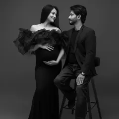This black and white portrait captures a quiet moment of connection. The expecting mother in a dramatic black ruffled gown looks at her partner with a gentle smile, creating a sophisticated and timeless fine art maternity photograph.