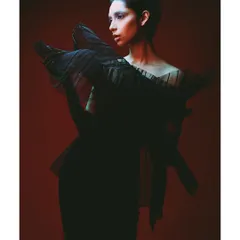 A shot from the 'Athena' series featuring a sculptural black dress against a fiery red background. The styling is avant-garde, and the lighting from the side carves out the model's silhouette.