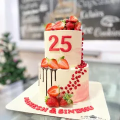 A fresh and vibrant two-tiered cake celebrating a 25th anniversary. This design features a chocolate drip, fresh strawberries, and a cascade of pomegranate seeds for a pop of color and flavor.