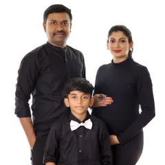 A chic and timeless family maternity portrait. The coordinated black outfits create a sophisticated look against a simple background, focusing on the family's connection.
