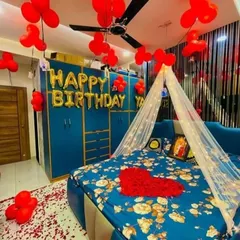 A beautiful birthday surprise for your loved one. This bedroom decoration includes red balloons, a heart made of rose petals on the bed, a light-up canopy, and "Happy Birthday" foil letters.