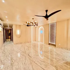 An expansive living room designed for openness and flow. The glossy marble floor reflects the custom wall lighting and sculptural ceiling fans, making the space feel vast and airy. This is a canvas waiting for life, designed with minimalism to maximize the feeling of calm.