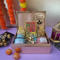 This elegant Diwali hamper comes in a textured pink box. It's filled with a scented candle, dry fruit potlis, gourmet cookies, and chocolates, making it a thoughtful gift for friends, family, or colleagues.