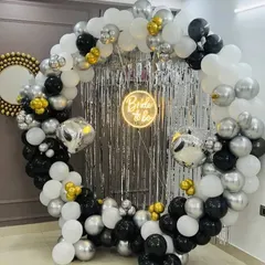 A chic 'Bride to be' party with a circular balloon arch in black, white, and silver, set against a shimmer curtain.
