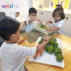 Three toddlers are fully engaged in washing cucumbers and carrots. These simple, purposeful tasks help develop their concentration and fine motor skills.