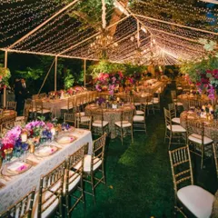 A breathtaking outdoor evening reception under a canopy of fairy lights. The long tables are beautifully set, creating a magical and grand setting for a large celebration.