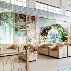 A cozy lounge nook with beige sofas set against a backdrop of artistic panels depicting a serene fountain scene.