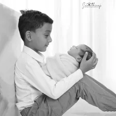 There's a special bond when a child becomes a big brother. This black and white portrait strips away all distractions, focusing solely on the gentle way he holds his new baby sibling. It’s a timeless image of growing love.