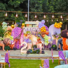 A vibrant and bold jungle theme for a second birthday, featuring a large stage with realistic animal props, including a lion and a purple-spotted giraffe, set in an outdoor space.