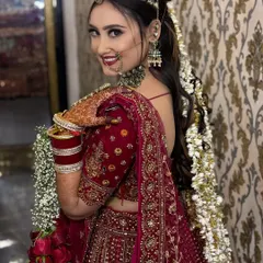 A happy bride, ready for her big day. This over-the-shoulder shot showcases her beautiful smile, flawless makeup, and the intricate details of her red lehenga and floral hair accessories.