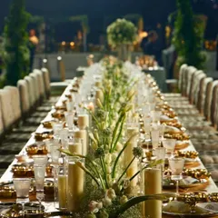 A breathtaking long table setup for an outdoor evening event. Lined with candles and white florals, it creates an intimate and magical atmosphere for a sit-down dinner under the stars.