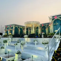 A frontal view of the royal stage, highlighting the central mandap structure and symmetrical design. The decor features elegant arches, floral embellishments, and soft lighting to create a romantic focal point.