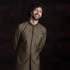 A smiling shot of the olive green sherwani-style kurta. The addition of a patterned pocket square adds a touch of personality to this minimalist and sophisticated ensemble.