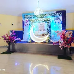A dreamy baby shower setup with a celestial theme. The stage features a large illuminated crescent moon, character cutouts, and soft blue lighting to welcome the baby-to-be.
