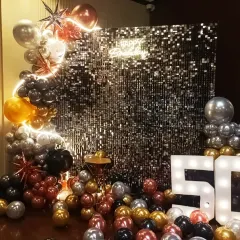 A glamorous 50th birthday photo booth featuring a black sequin wall, a 'Happy Birthday' neon sign, marquee numbers, and a balloon arrangement in silver, gold, and black.