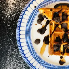 A classic chocolate chip waffle, artfully captured from above. The dusting of powdered sugar and drizzled chocolate sauce adds texture and a sense of indulgence to this dessert shot.