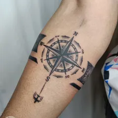 A travel-themed armband tattoo featuring a compass. The compass points are integrated into a geometric band, symbolizing a love for adventure and always finding your own direction.