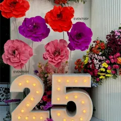The light-up marquee '25' next to a display of giant paper flowers, creating a perfect photo corner.