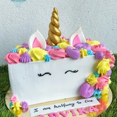 A magical unicorn-themed half-birthday cake. This design features a colorful mane of whipped cream swirls and a golden fondant horn, perfect for a six-month celebration.