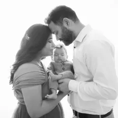 A timeless black and white portrait capturing the quiet, tender moment of new parents embracing their newborn. This is the beginning of your family's story.