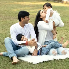 A candid and playful family moment on the grass, with mom kissing the baby while dad and brother look on with love.