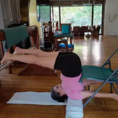 This is not a relaxation pose; it is an active, supported inversion using chairs. This setup allows the spine to lengthen and the chest to open, calming the nervous system and improving circulation without any pressure on the neck.
