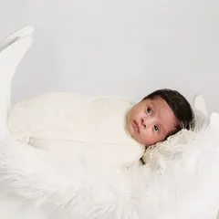 A serene portrait of an awake newborn resting in a white moon prop. The simple, all-white setup with soft fur creates an angelic and dreamy atmosphere.
