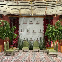 This 'Divya Stambh' setting reimagines a South Indian temple sanctum. The stage features authentic temple pillars, lush mango trees, and walls of red roses, all set against a backdrop of niches holding sacred brass figurines.