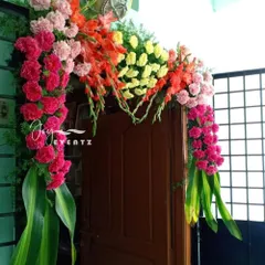 A vibrant floral arch for a flat's main door, perfect for a housewarming. We used a mix of pink and red carnations, gladiolus, and lush green leaves to create a full and colorful welcome.