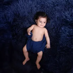 A minimalist portrait focusing on the baby's sweet expression. The simple setup with a deep blue, fluffy rug creates a beautiful contrast and keeps the focus on the child.