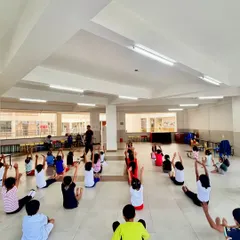 This is what a full class looks like. I guide a large group of children through seated stretches, ensuring everyone participates and learns together.