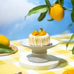 A whimsical mango mousse dessert on a pedestal, set against a dreamy blue sky backdrop with a mango branch. This conceptual shot creates a surreal summer picnic vibe, perfect for a seasonal menu.