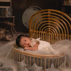 A full-length shot of a newborn resting in a rustic, rainbow-shaped cane bassinet. The setup includes soft tulle and star-shaped pillows, creating a dreamy and safe space for the baby's first photoshoot.