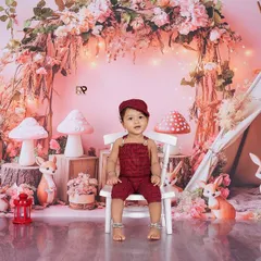 A baby boy sits on a chair in a beautiful pink-toned woodland scene. The floral arch, teepee, and deer figures make this a truly magical and enchanting portrait.