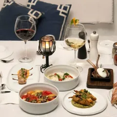 A beautiful spread of our small plates, featuring lamb chops, fish in a creamy sauce, and a vibrant tomato salad, ideal for a tasting experience.