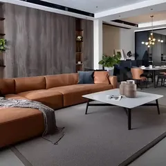 We designed this open-plan living and dining area with a cohesive aesthetic. The space features a comfortable tan leather sectional sofa, a minimalist coffee table, and dark wood paneling that adds warmth and texture.