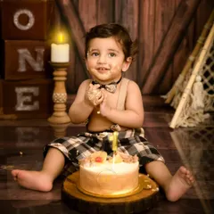 A joyful one-year-old boy enjoying his cake smash, with cake on his face and a big smile. This rustic, woodland-themed setup is perfect for a little adventurer.
