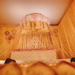 Here is the full view of the beautiful Haldi ceremony stage I designed. The setup features a canopy of hanging floral strings, a tiered seating area with a chevron pattern, and a large brass uruli in the front for the rituals.