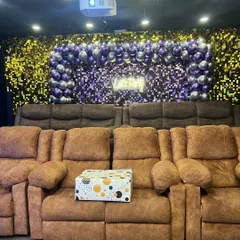 A look at one of my classic theater setups. It features comfortable brown recliner sofas, a sequin and balloon backdrop, and a "Let's Party" neon sign, ready for you to bring your friends and have a great time.