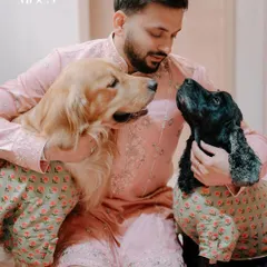 A groom shares a quiet moment with his two beloved dogs, a golden retriever and a cocker spaniel, both dressed in matching festive attire. We believe pets are family, and we love capturing these special bonds during your most important life events.
