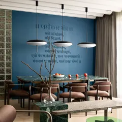 The dining area, where a green Indian marble table is set against a deep blue wall featuring a Jain mantra. The mantra's letters are finished in the same tone as the wall, creating an understated yet powerful spiritual element in this modern space.