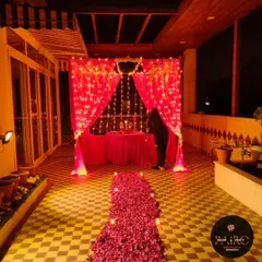 A terrace transformed for a Valentine's dinner, with a red curtained backdrop, fairy lights, and a long pathway made of red rose petals.