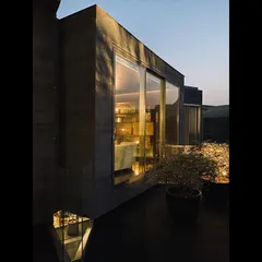 The warm interior light glows from a window of the Jenga House at dusk. This detail highlights the contrast between the solid concrete exterior and the life within the home.